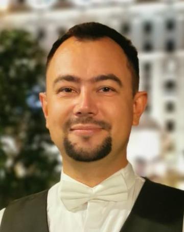 A head shot of Vlad wearing a white bow tie, formal shirt and grey waistcoat, he is looking straight ahead, smiling slightly